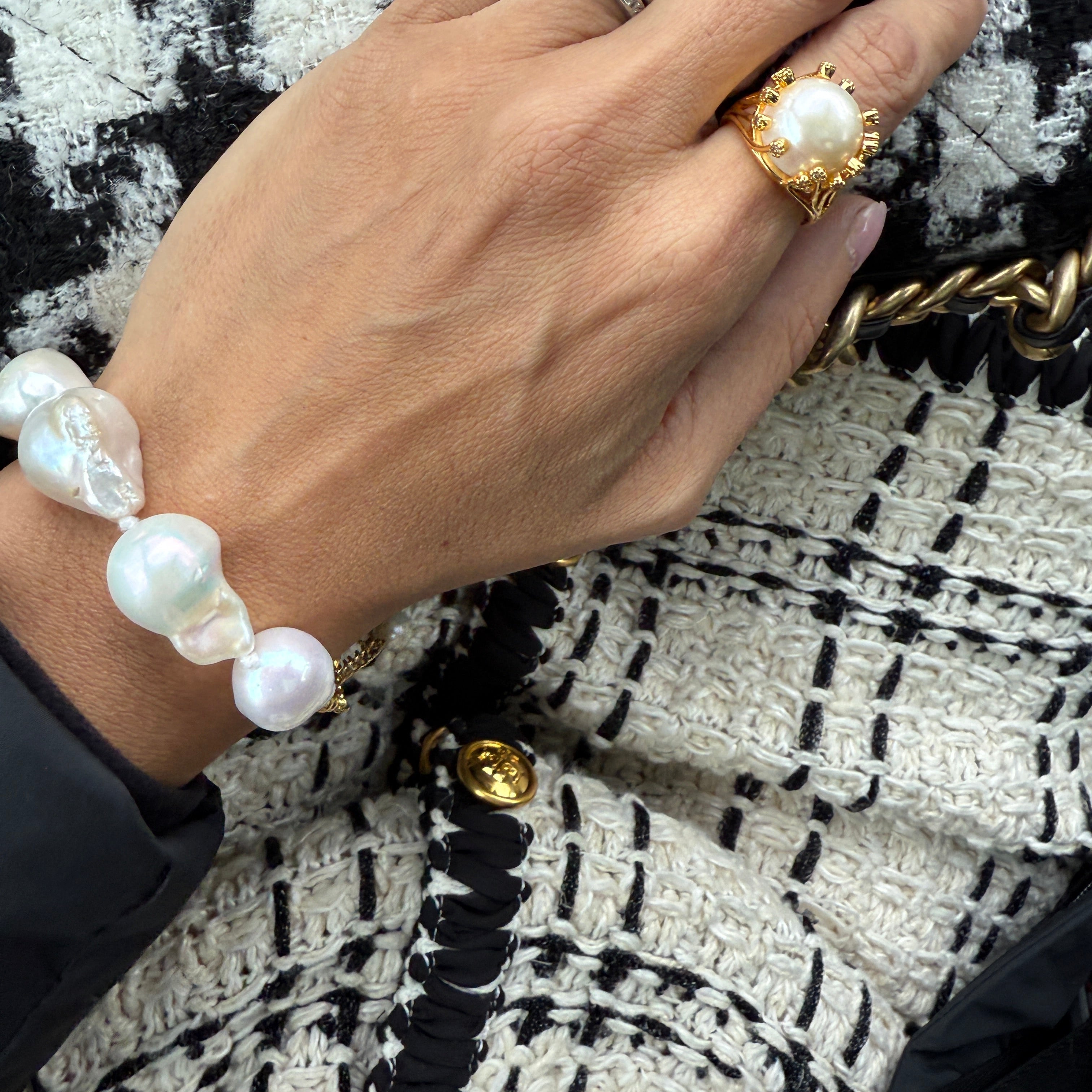Hand wearing a gold ring and pearl bracelet on a patterned fabric background